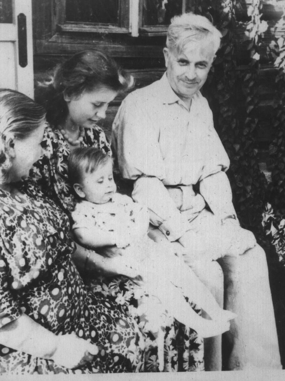 Группа людей сидит на природе, среди них мужчина средних лет в белой рубашке